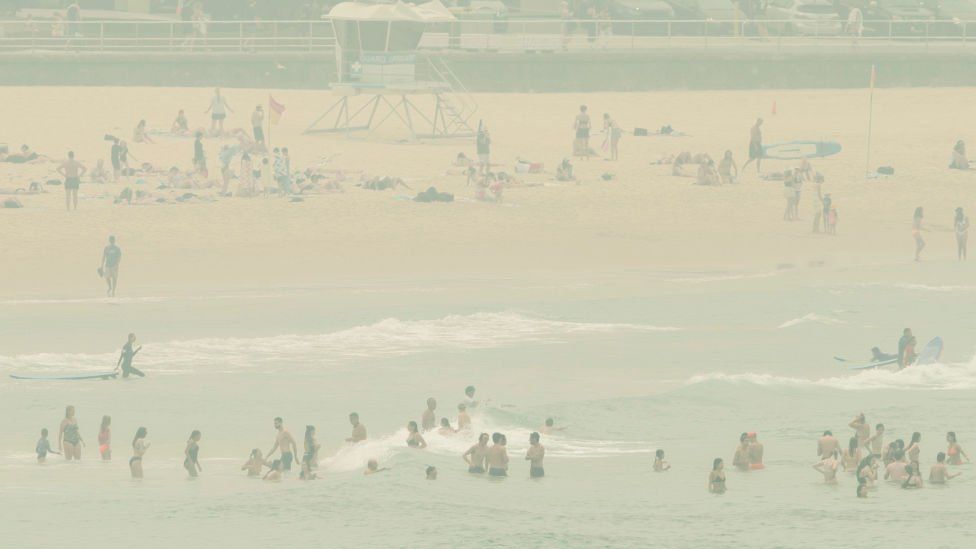 Beachgoers on Bondi Beach amid a heavy smoke haze,