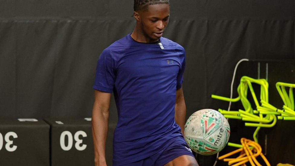 Kelvin Akwasi in blue football kit, kicking up the football on his knee