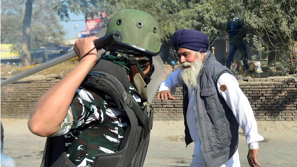 A police officer raises his baton to hit an Indian farmer