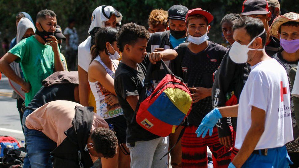 Venezuelan migrants wear a face masks as they queue to receive food and medicines from members of the Red Cross on a highway in Cucuta