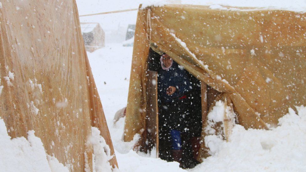 A Syrian refugee stands at the entrance of a tent during a snowstorm at camp in Lebanon