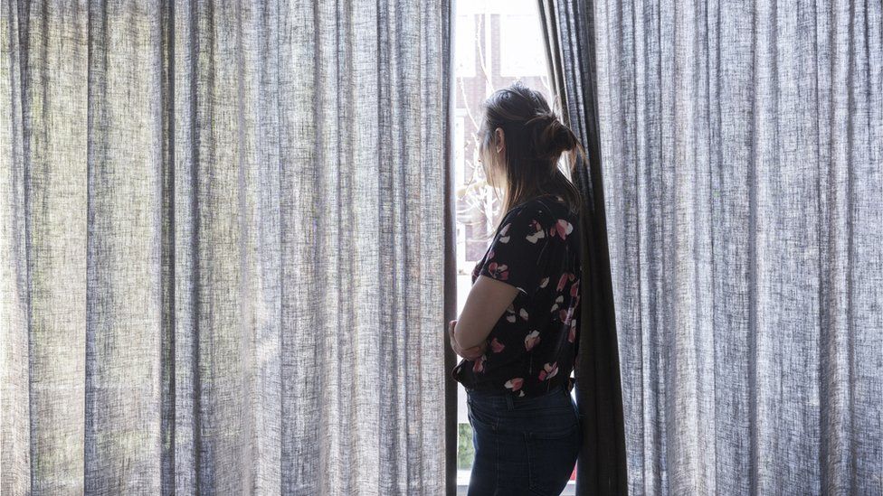 A woman looking out of her window between drawn curtains