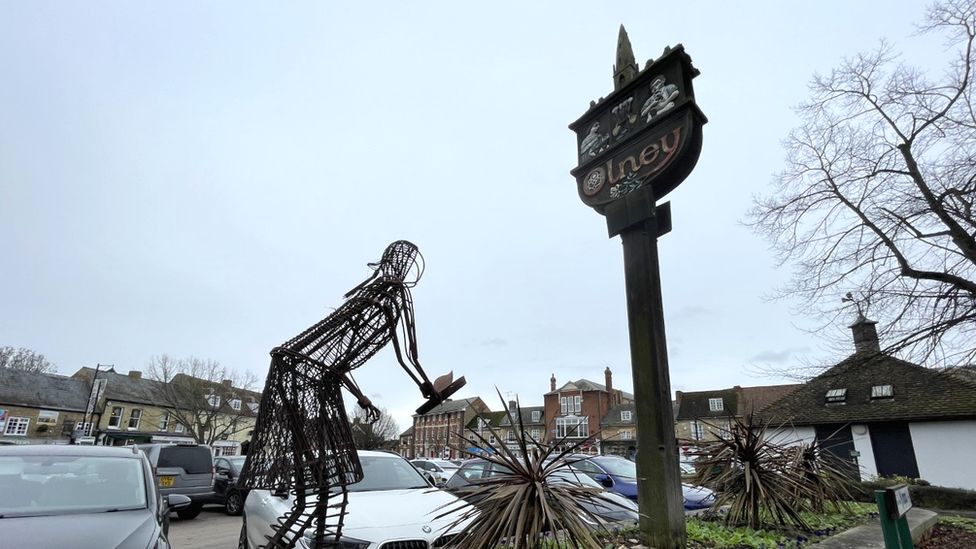 An Olney sign, with a sculpture depicting the town's pancake race