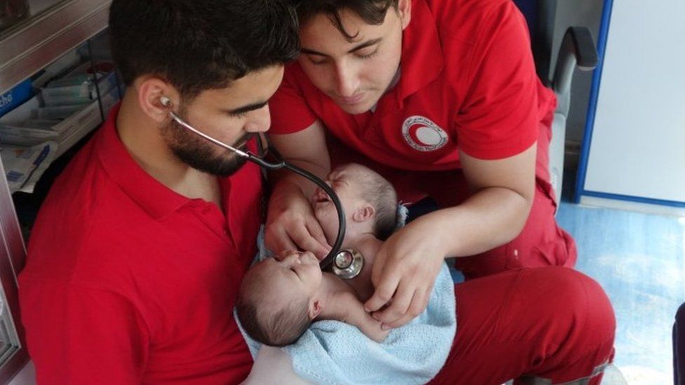 Syrian Arab Red Crescent medics hold conjoined twins Nawras and Moaz before evacuating them from Douma (12 August 2016)