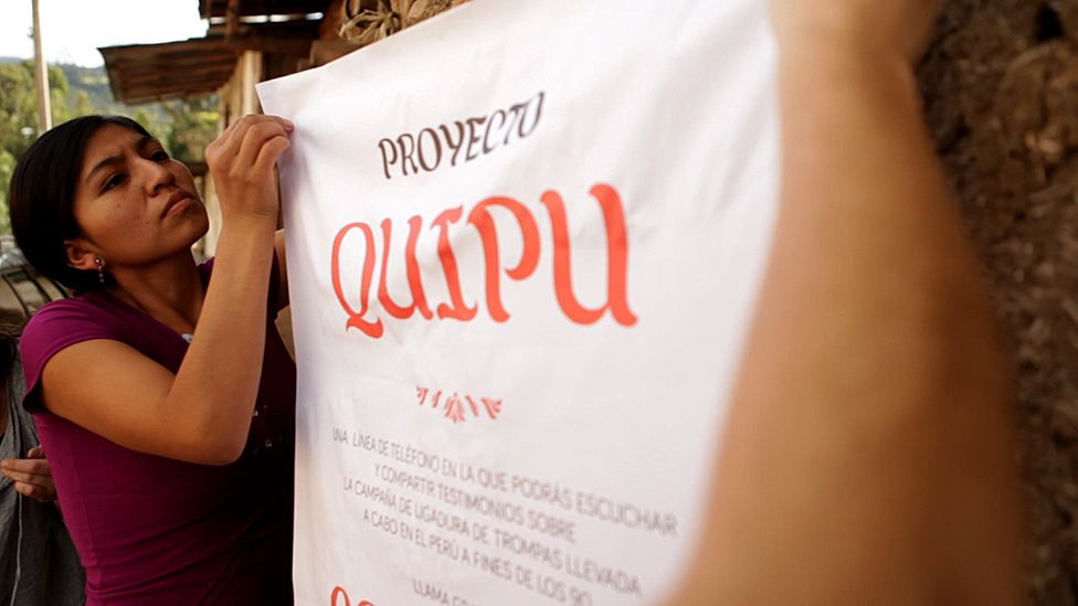 A woman putting up a banner advertising the Quipu project