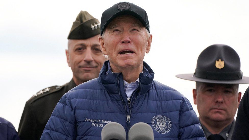 Biden in blue jacket, black cap