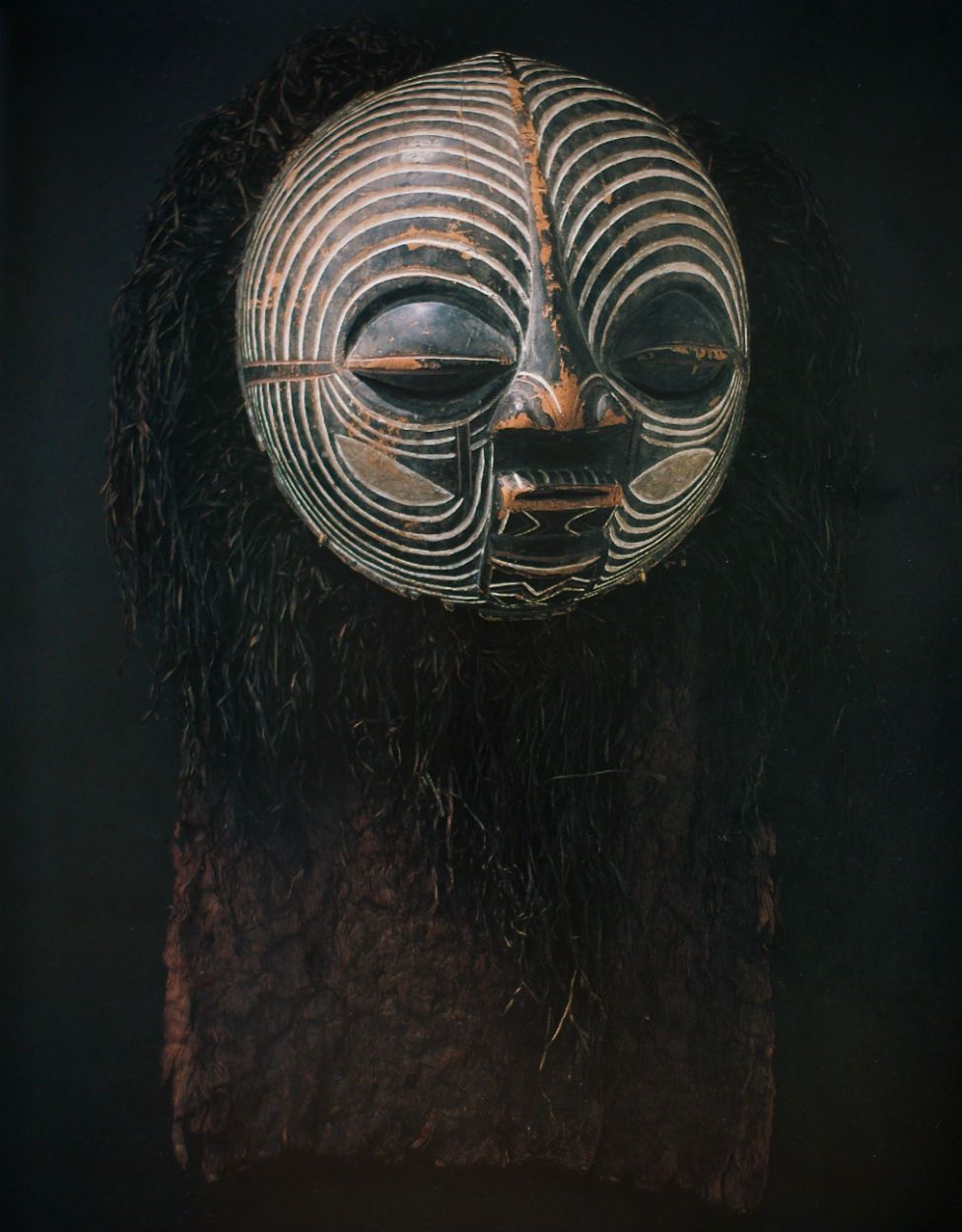 A mask of sculpted wood, pigment, hair and natural fibres.