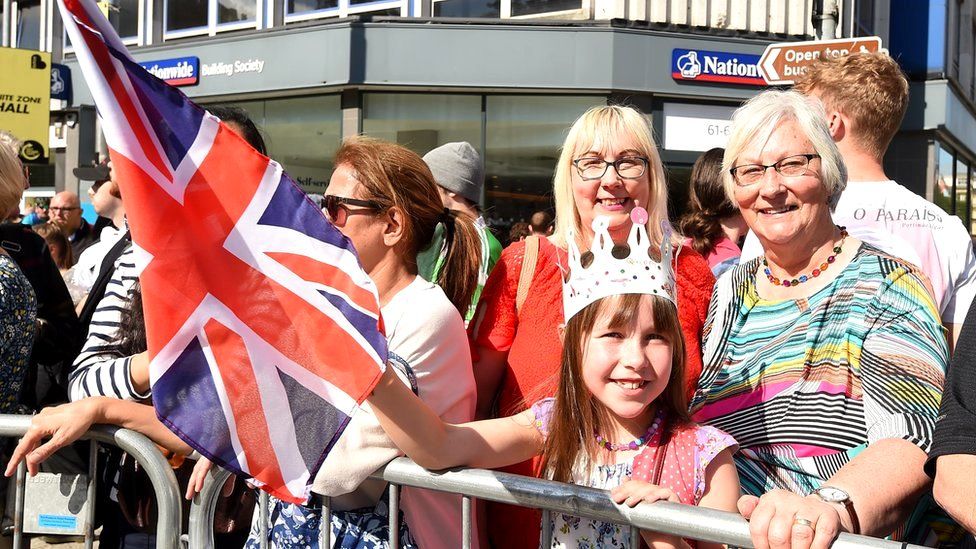 A girl wears a paper crown and holds a Union flag as she stands with her mother and grandmother outside Belfast City Hall as they wait for the King and Camilla to pass by on their way to St Anne's Cathedral