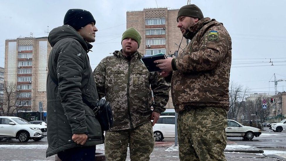 Conscription officers speak to a man on a street in Cherkasy