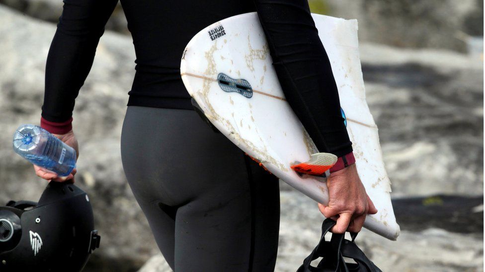 a person in a wetsuit carrying part of a broken surfboard
