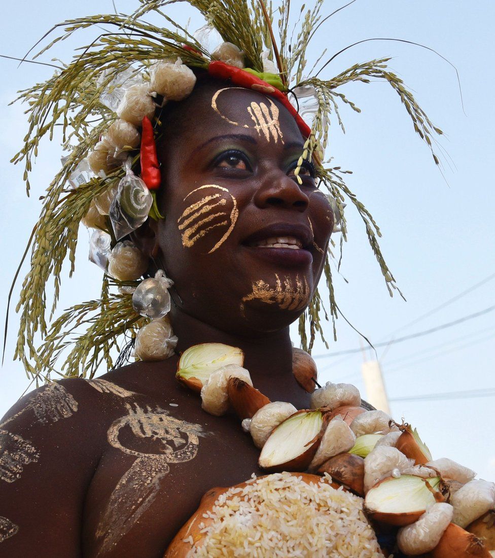 A woman with a necklace made out of onions and a head dress featuring corn and red peppers in Grand-Bassam, Ivory Coast - Sunday 20 November 2016