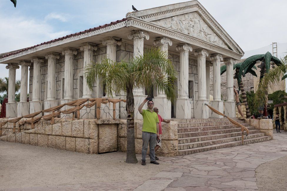 A man takes a selfie outside a Roman style building