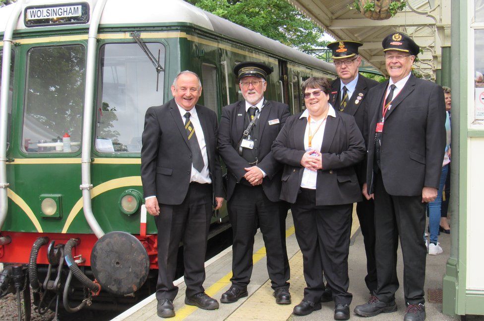 Five staff in uniform stand next to a train