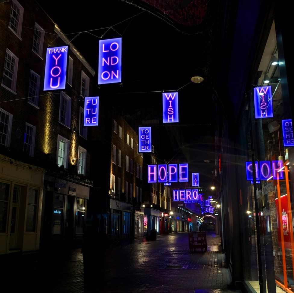 An image of a street at night with lots of lit hanging signs saying messages