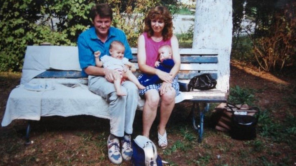 Adi in the arms of her adoptive Dad, sitting next to her adoptive Mum