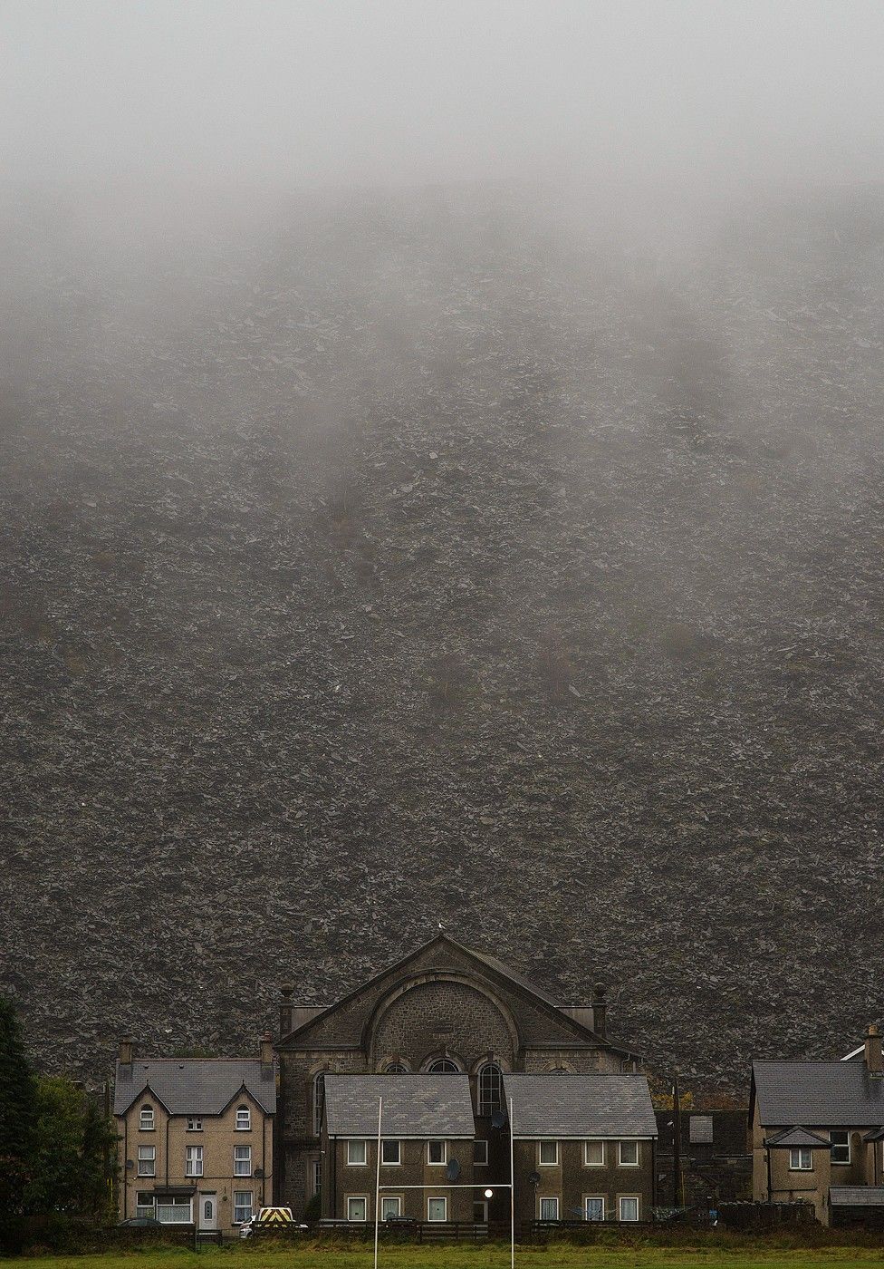 A chapel and a collection of houses with a huge slate mountain behind them