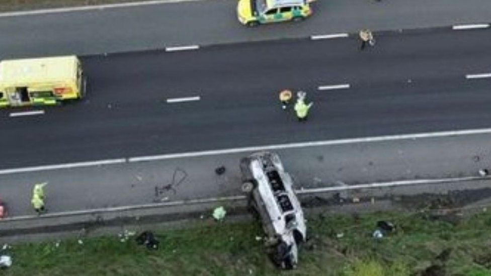 Over turned bus on the side of the motorway with emergency workers standing nearby
