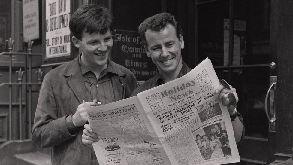 Black and white photograph of two men looking at a newspaper