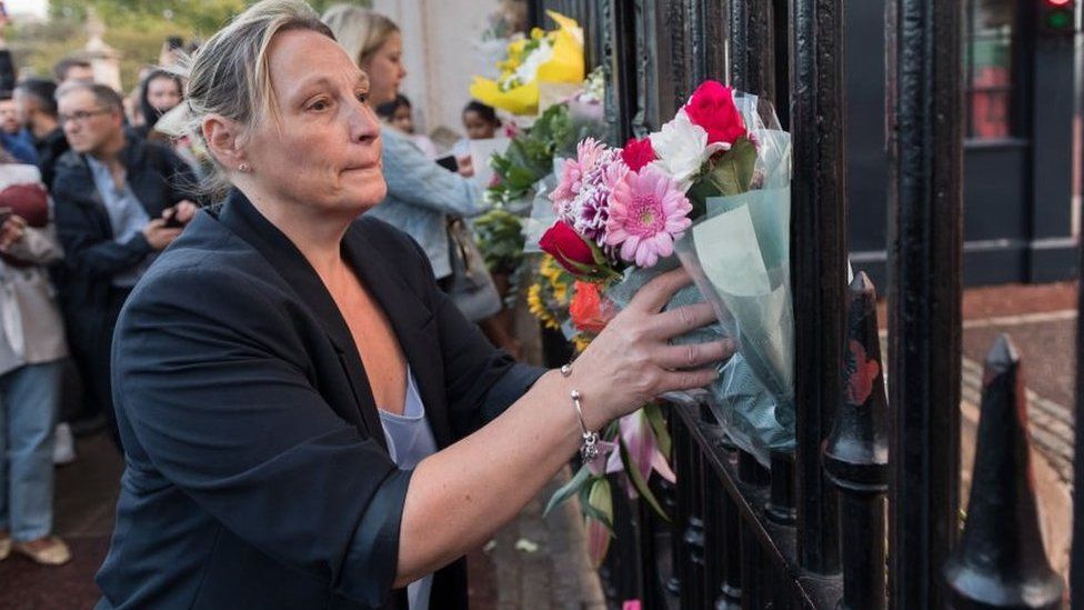 A woman places flower tributes at the gate of Buckingham Palace