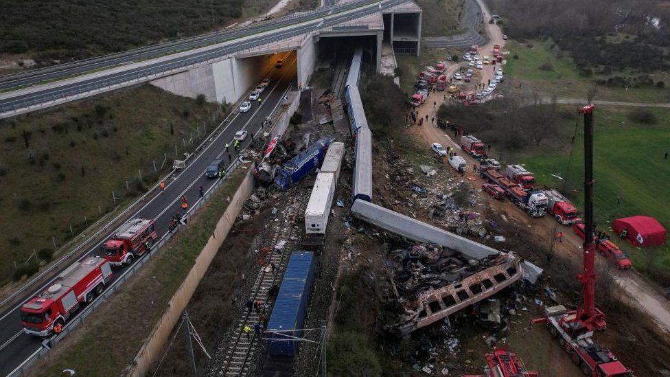 An aerial image shows the derailed trains in the daylight