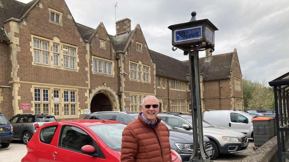 Martin Johns in front of the former police station. The 1930s building is red brick and Mr Johns is standing next to an iron pole with a dark blue police sign at the top.