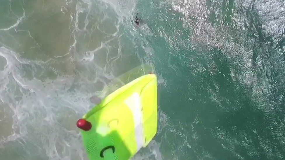 A screengrab from the drone's recorded footage shows it drop a yellow inflatable rescue device into the sea to help the struggling teenagers