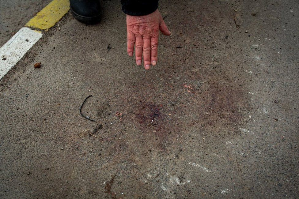 Volodymyr Abramov points to the spot on the pavement outside their house where he says his son-in-law was forced to kneel and shot in the head