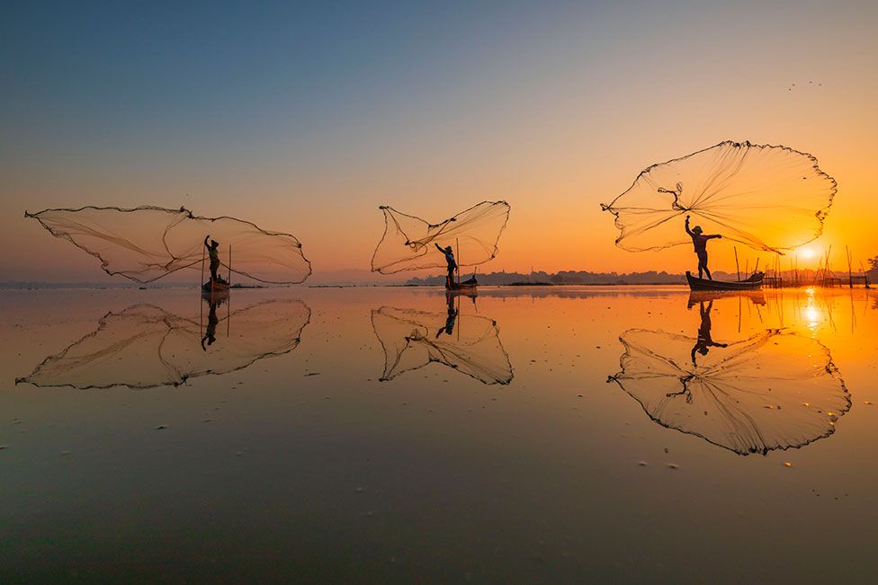 Three fisherman throwing their nets out to sea with a sunset behind them