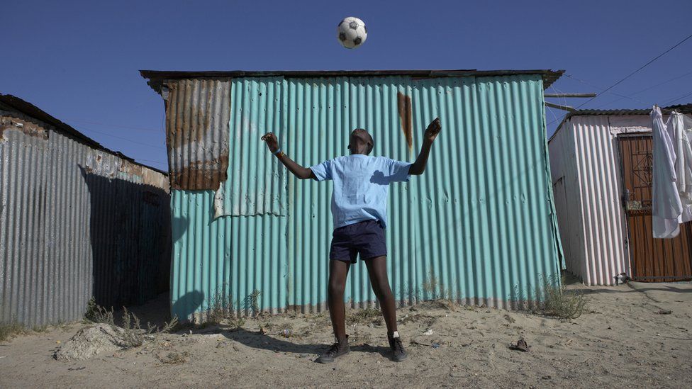 Мальчик играет в футбол в городке в Кейптауне, Южная Африка