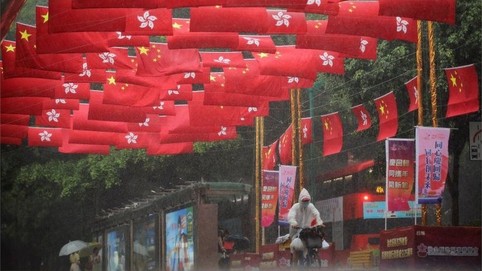 Велосипедист едет под дождем под китайскими и гонконгскими флагами, украшающими улицу, перед 25-й годовщиной передачи бывшей британской колонии китайскому правлению в Гонконге, Китай, 30 июня 2022 г.
