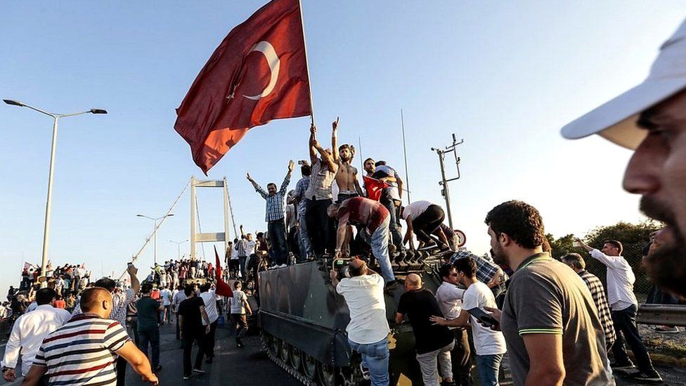 People standing on a tank with a Turkish flag