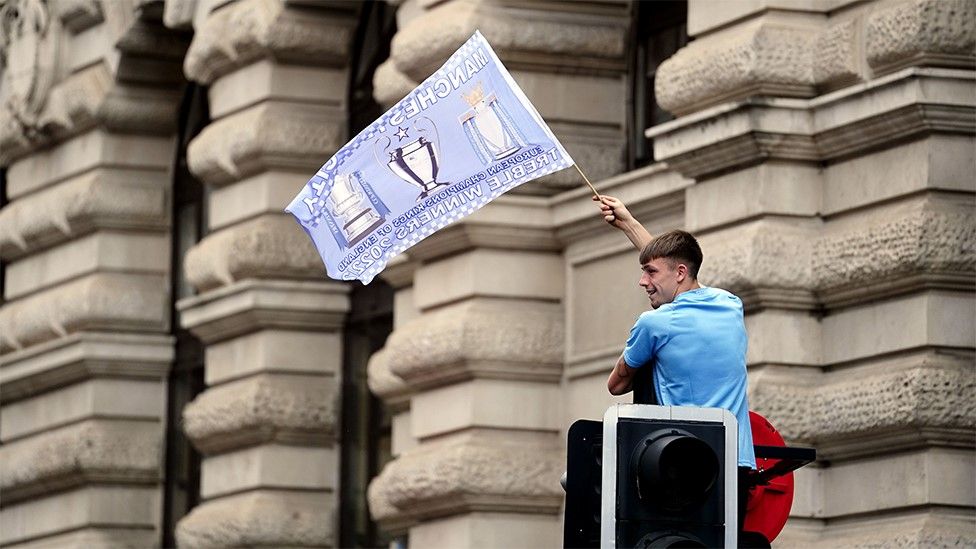 Manchester City fan sitting on a traffic light waving a flag