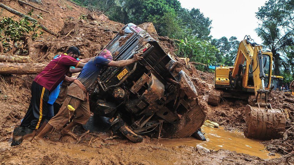 Rescue workers push an overturned vehicle stuck in the mud and debris at a site of a landslide said to have been caused by heavy rains in Kokkayar in India's Kerala state, 17 October 2021