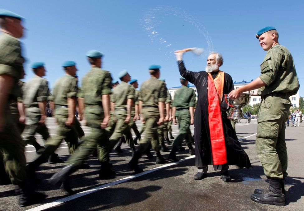 A priest sprays water as troops walk by