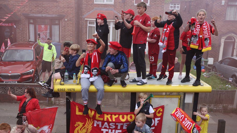 Liverpool fans celebrate on top of a bus stop during the bus parade