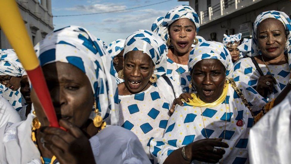 Women dressed in a patterned white a blue outfit with horn blowers. They are celebrating