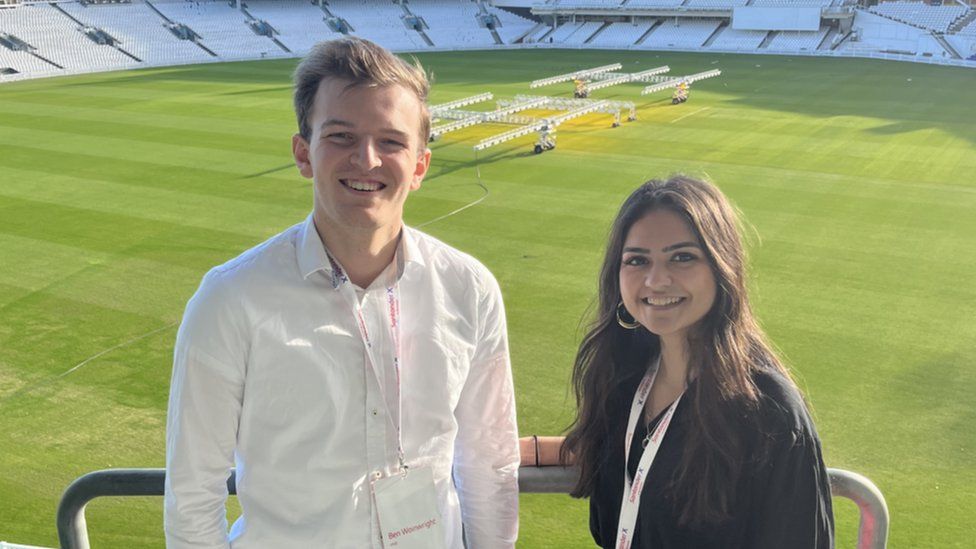A pair pf young people in front of a cricket pitch