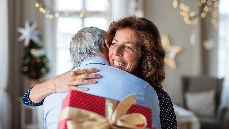 Portrait of senior couple with Christmas present indoors, hugging. - stock photo