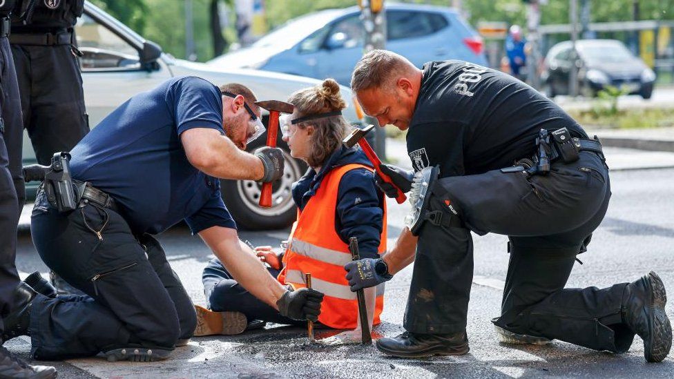 Полицейские работают над освобождением климатического активиста Letzte Generation (Последнее поколение) после того, как он приклеился к асфальту во время климатической акции протеста в Берлине, Германия, 22 мая 2023 г.