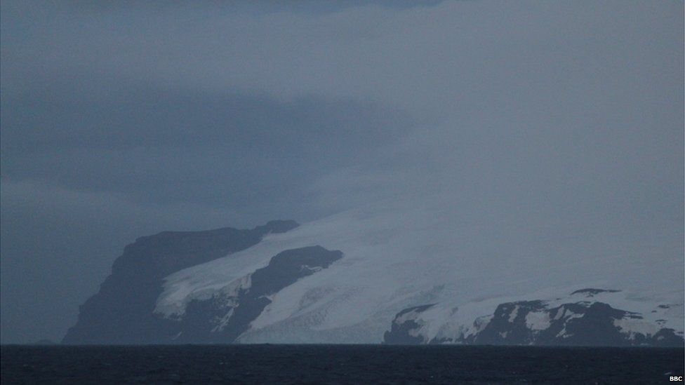 Bouvet Island in the foreground, surrounded by dark ocean waters and cloudy skies.