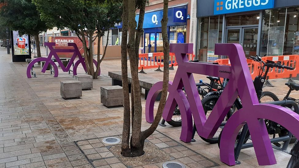 The two bike parks with metal frames made in the shape of large purple bicycles embedded in the street