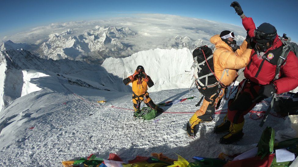 Sherpas and climbers standing on the summit of Everest