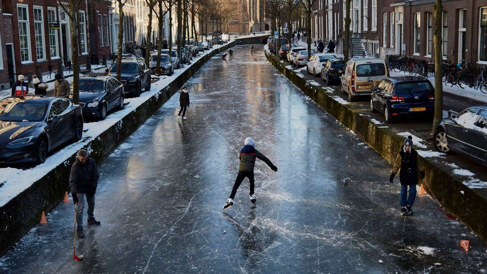People skate on a frozen canal in a residential area of the Netherlands