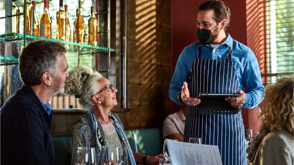 Man wearing face mask handing menu to woman, dining out, the new normal, weekend activities, food and drink