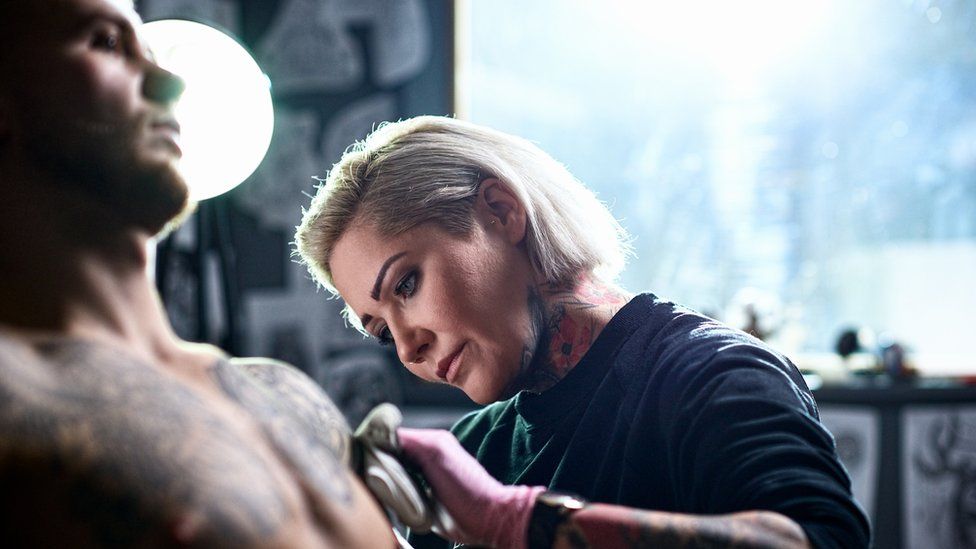 Female tattoo artist working on a male client