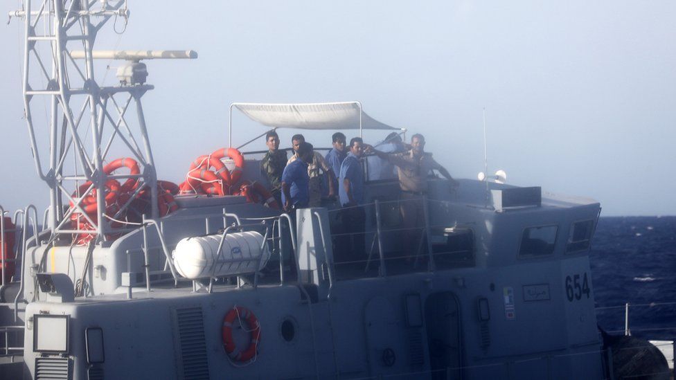 A Libyan coast guard officer aboard a vessel signals at former fishing trawler Golf Azzurro on 15 August