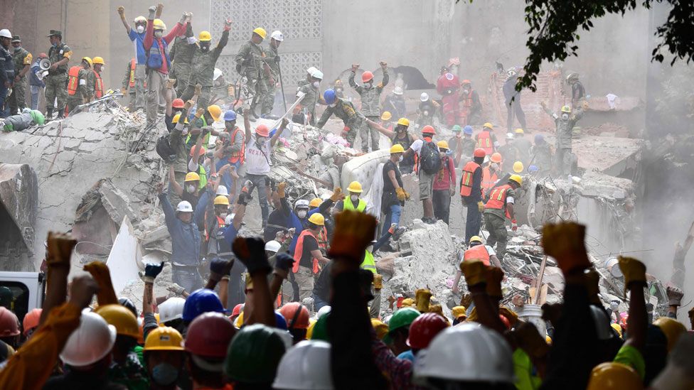 Rescuers raise their fists for silence at the site of a collapsed building in Mexico City