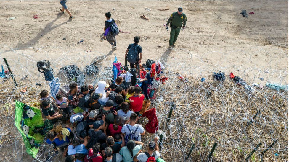 Um guarda de fronteira dos EUA observa migrantes entrando nos EUA