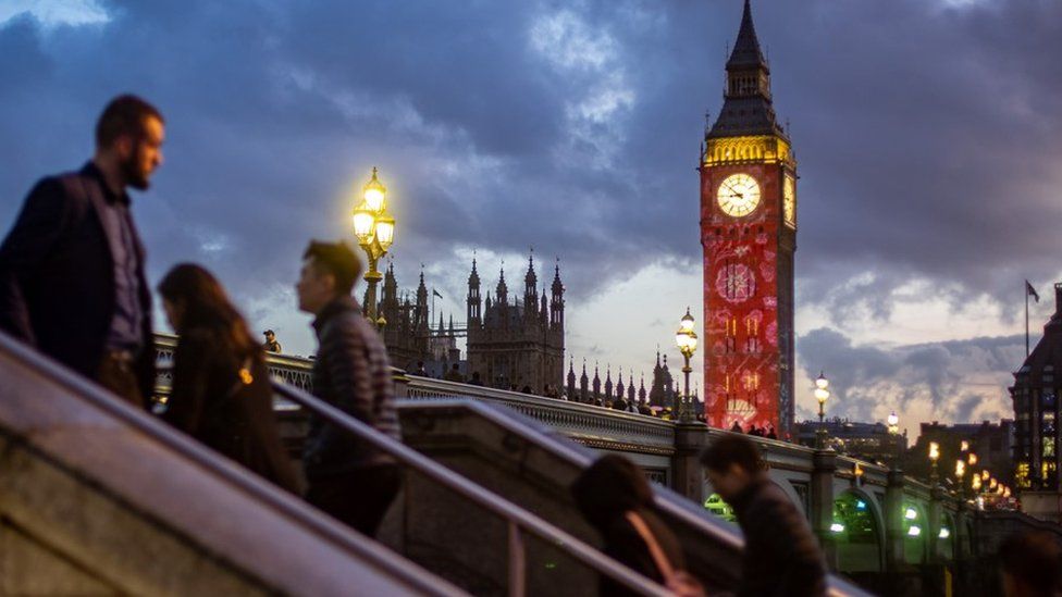 People walk near the Elizabeth Tower, that is illuminated with a series of projections to mark King Charles III's Coronation in London