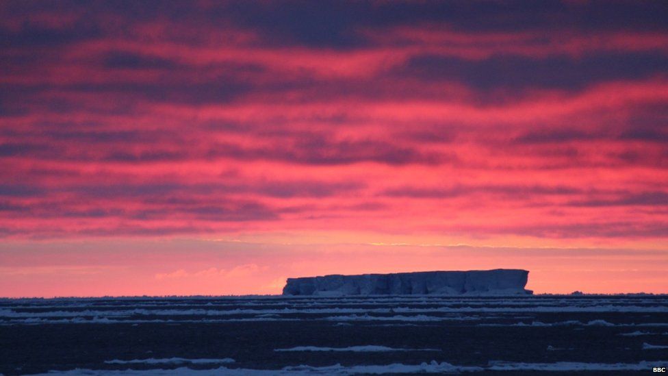 A bright pink and red sky, over a large iceberg